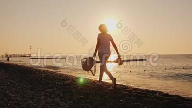 在黎明时分，手里拿着背包和帽子的无忧无虑的女人沿着海滨奔跑。 暑假概念